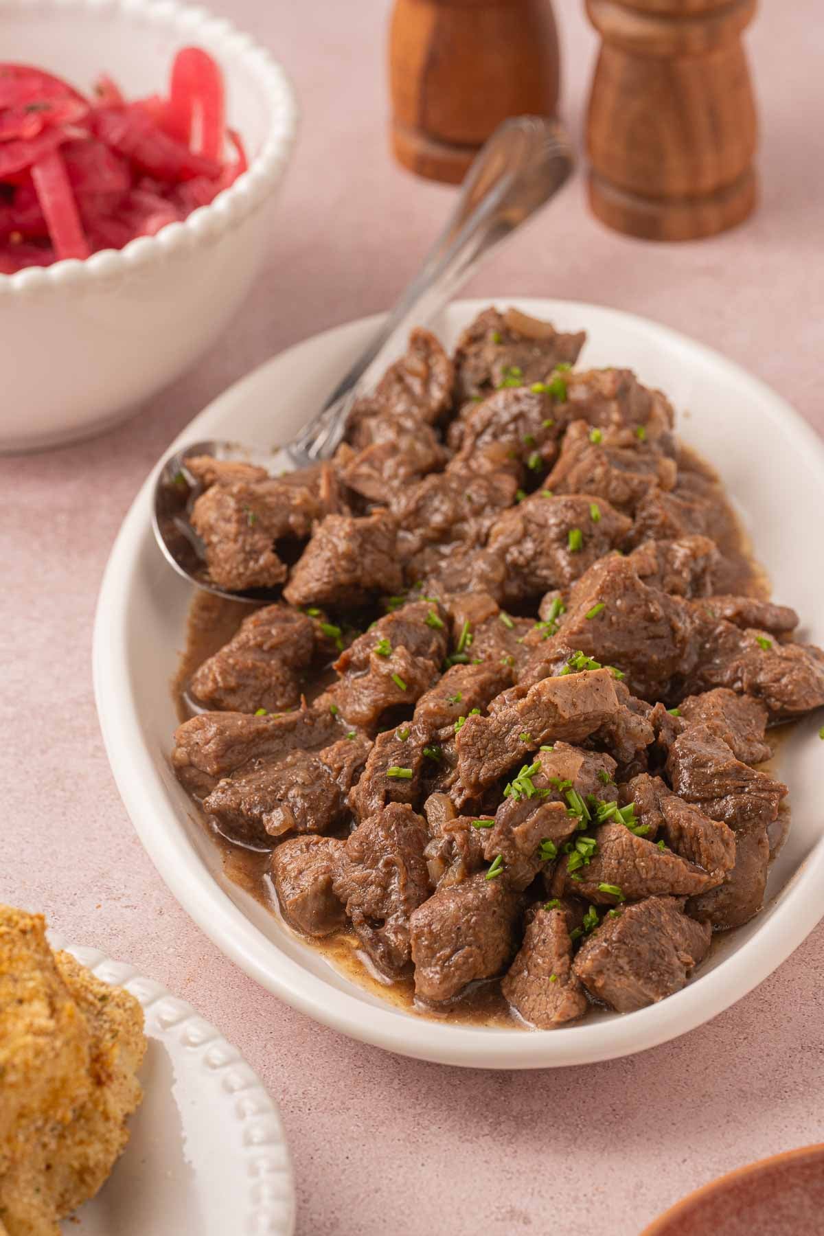 Sauerbraten beef on platter with gravy and picked onions.