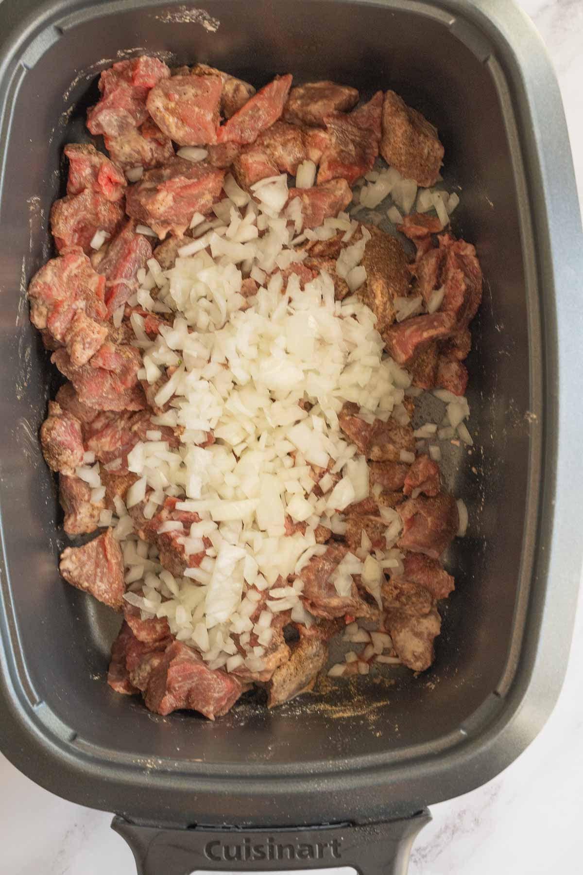 Flank steak cubes, onion and spices in slow cooker.