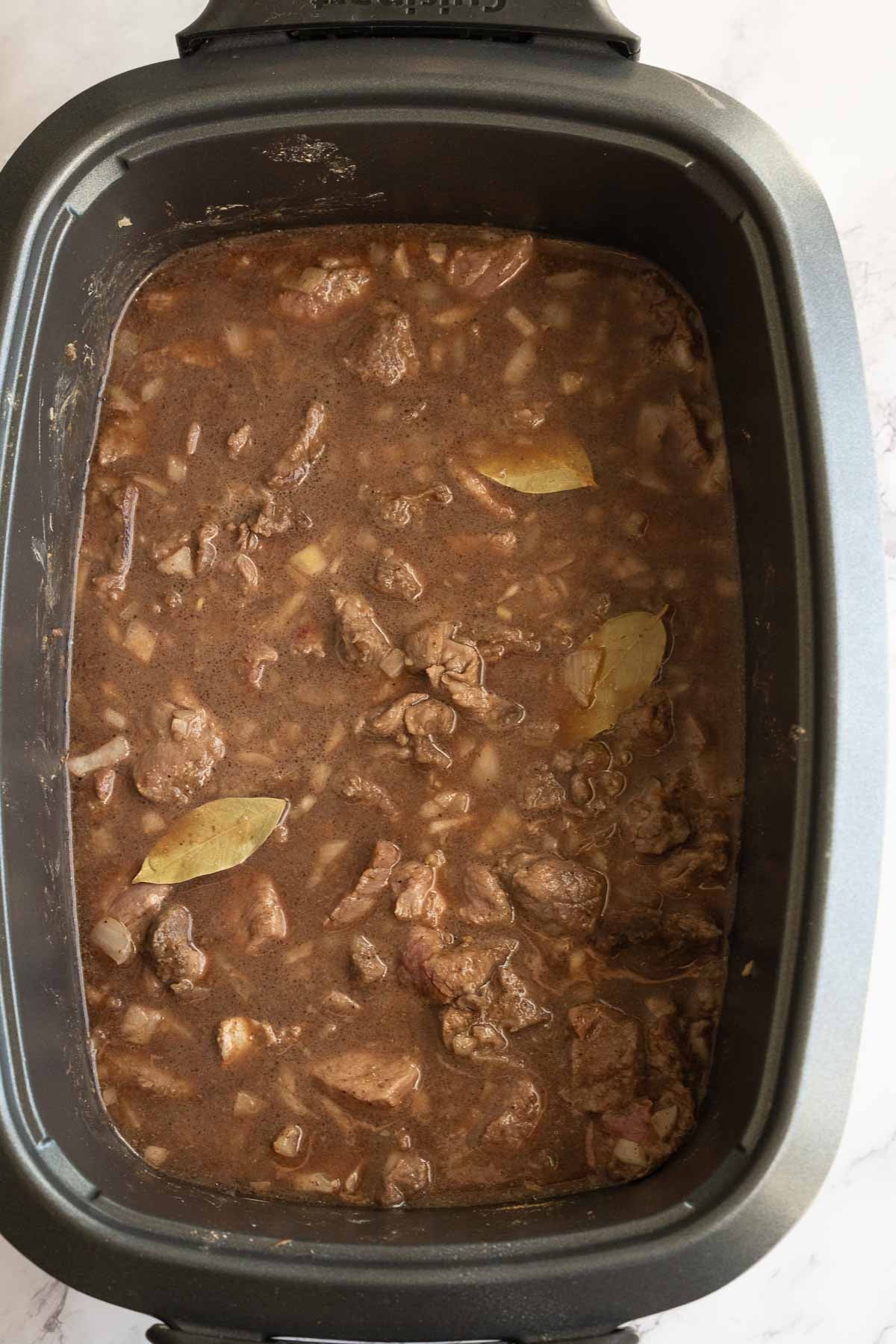 Sauerbraten beef with bay leaves and gravy in slow cooker.