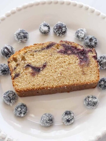 slice of blueberry swirl cake with sugared blueberries on white plate