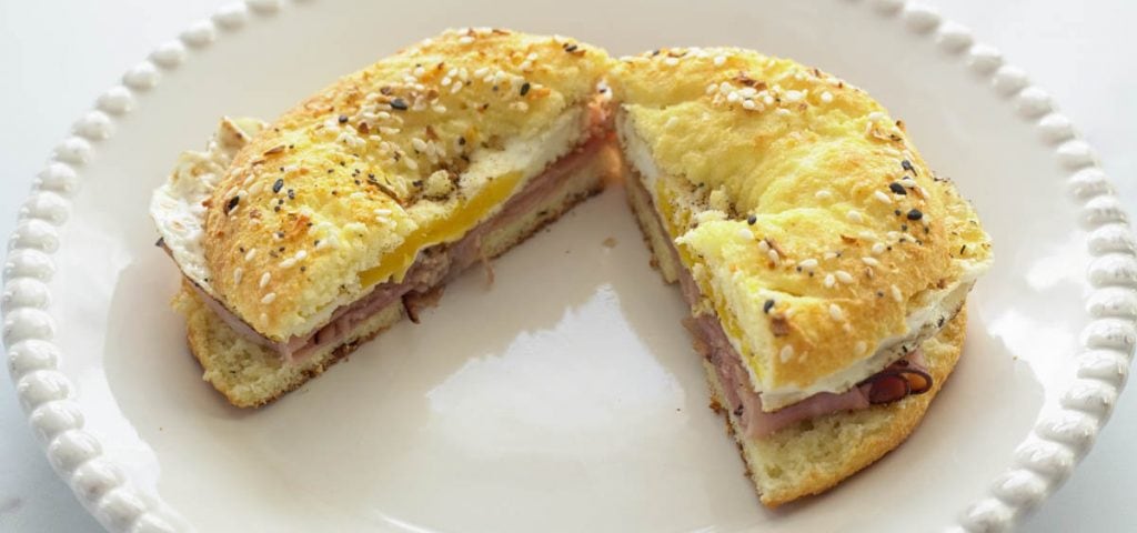 low carb breakfast  bagel sandwich of fried egg and ham sliced in half on white plate