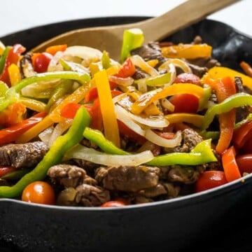 pepper steak and onions with tomatoes in a cast iron skillet