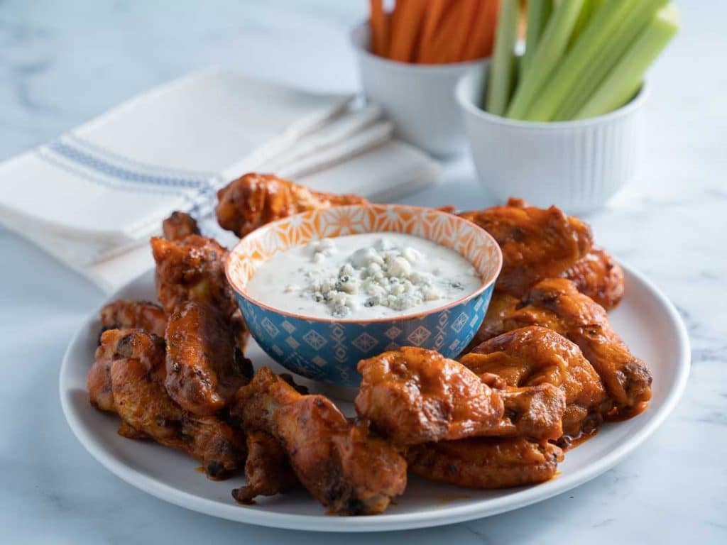 keto buffalo chicken wings on white plate with blue cheese dressing, carrots and celery