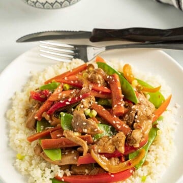 keto chicken stir fry with cauliflower rice on white plate with knife fork and striped napkin