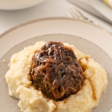keto salisbury steak with red wine gray over mashed cauliflower on dinner plate. Serving bowl of broccoli and carrots
