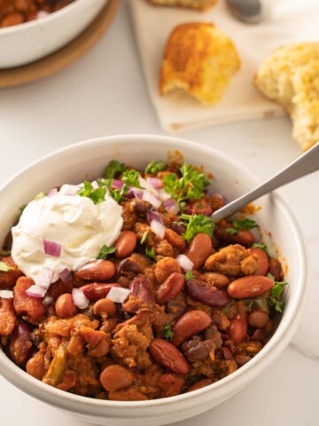 sausage chili with sour cream, onion, parsley in white bowl with corn muffin