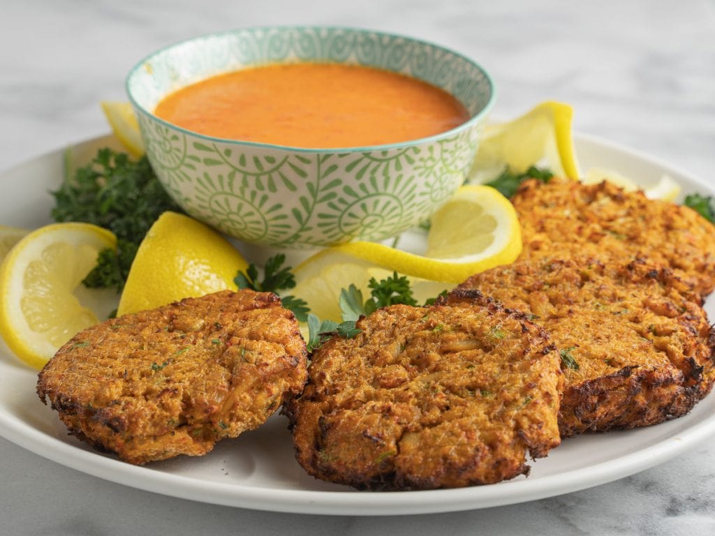 Air fryer crab cakes with sauce and lemons on white plate 