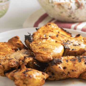 grilled chicken thighs on plate, coleslaw in glass bowl