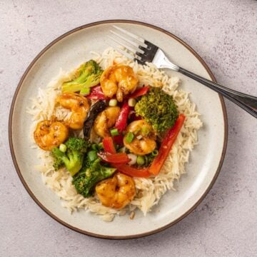 shrimp, broccoli, red pepper over cauliflower rice on beige plate with fork