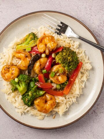 shrimp, broccoli, red pepper over cauliflower rice on beige plate with fork