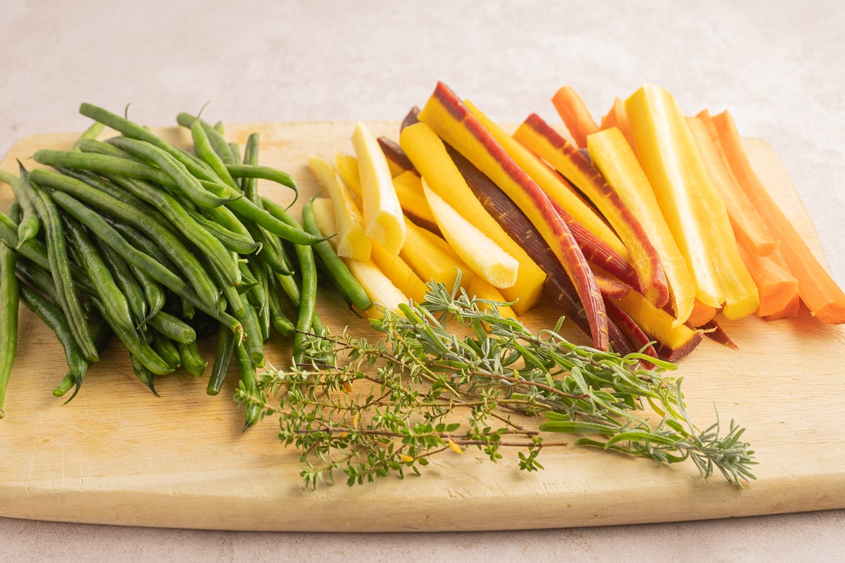 string beans, herbs, carrots on cutting board.