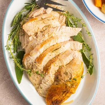sliced turkey breast, fresh herbs on white platter.