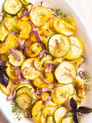 roasted zucchini, yellow squash, red onions, herbs on white platter.