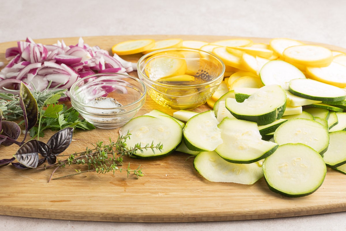 zucchini, squash, red onion, herbs, olive oil, seasonings on wood cutting board.