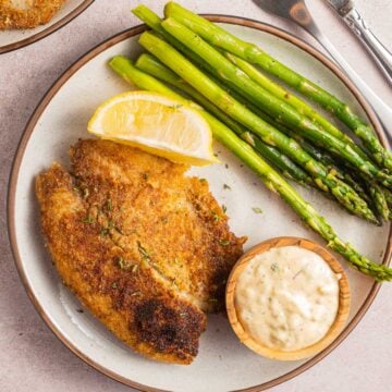 fried fish fillet, lemon, asparagus, tartar sauce on plate.