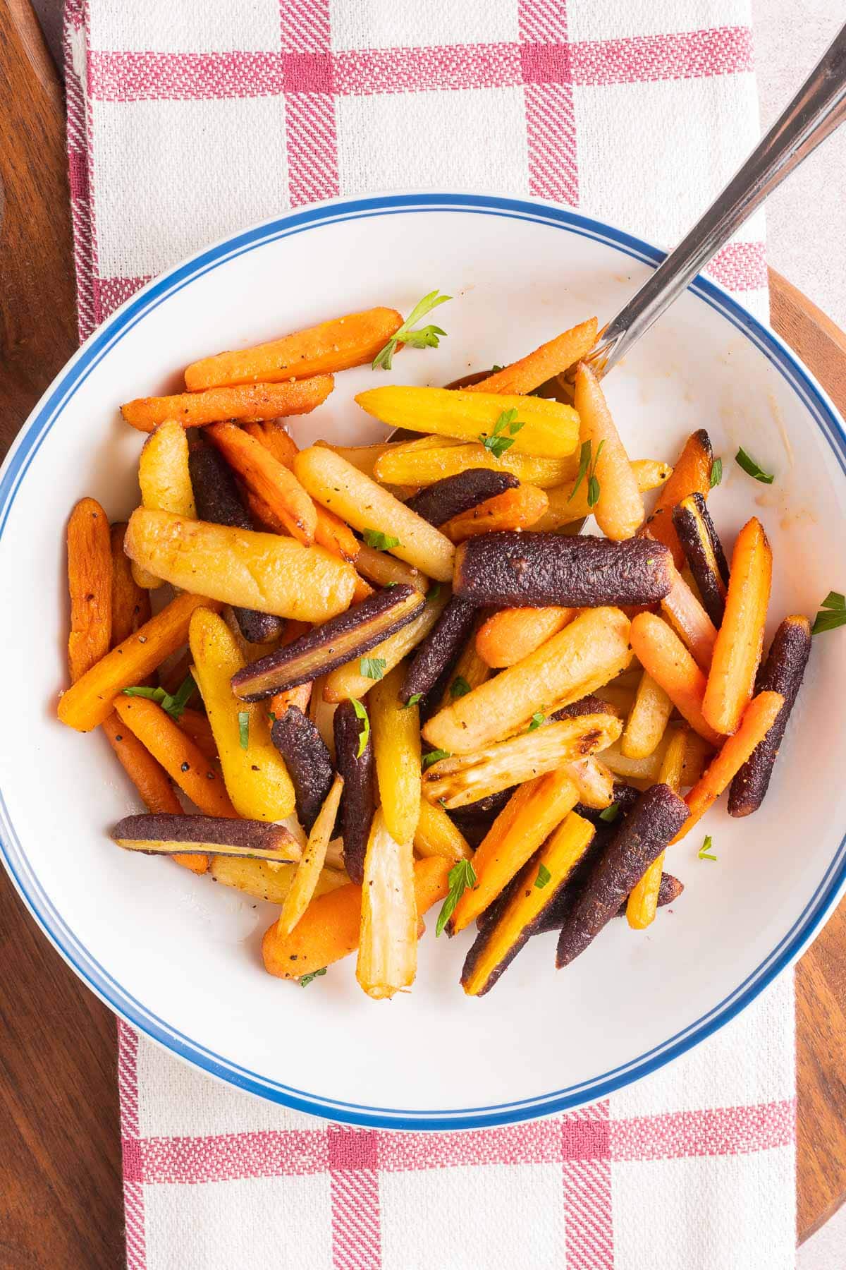 rainbow carrots in white bowl on wooden board.