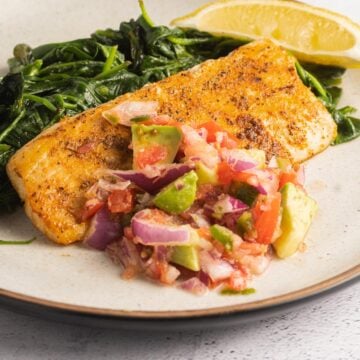 mahi mahi filet, spinach, lemon, salsa on plate.