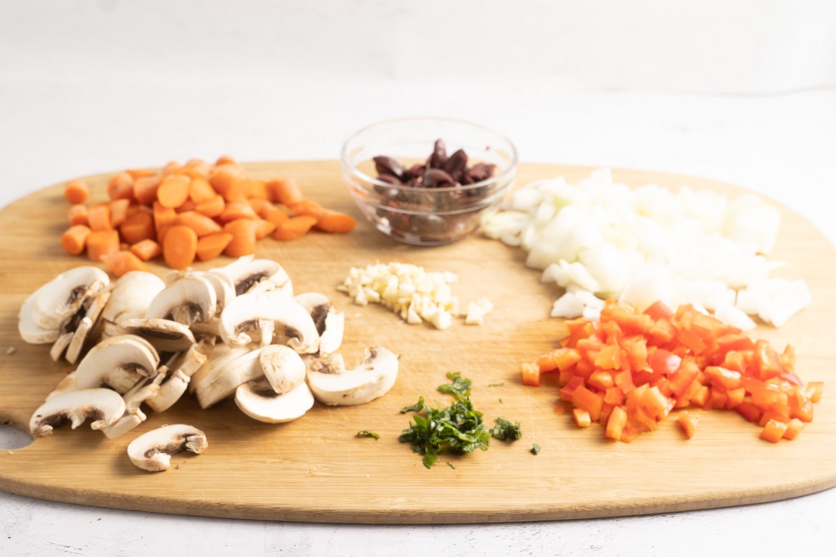 sliced mushrooms, carrots onions, olives, basil, red pepper on cutting board.