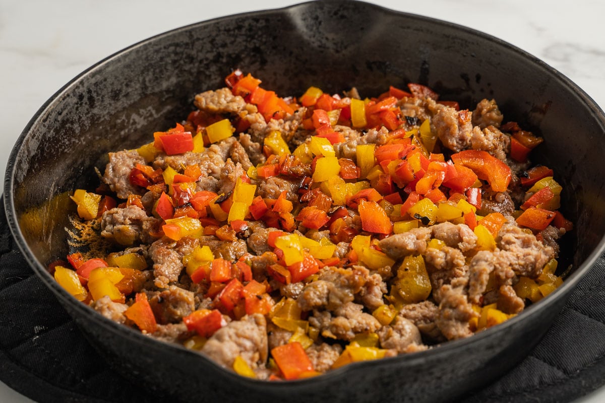 sausage, vegetables cooking in cast iron skillet.