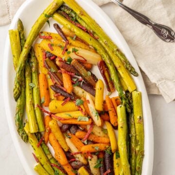 asparagus and baby carrots on white platter.
