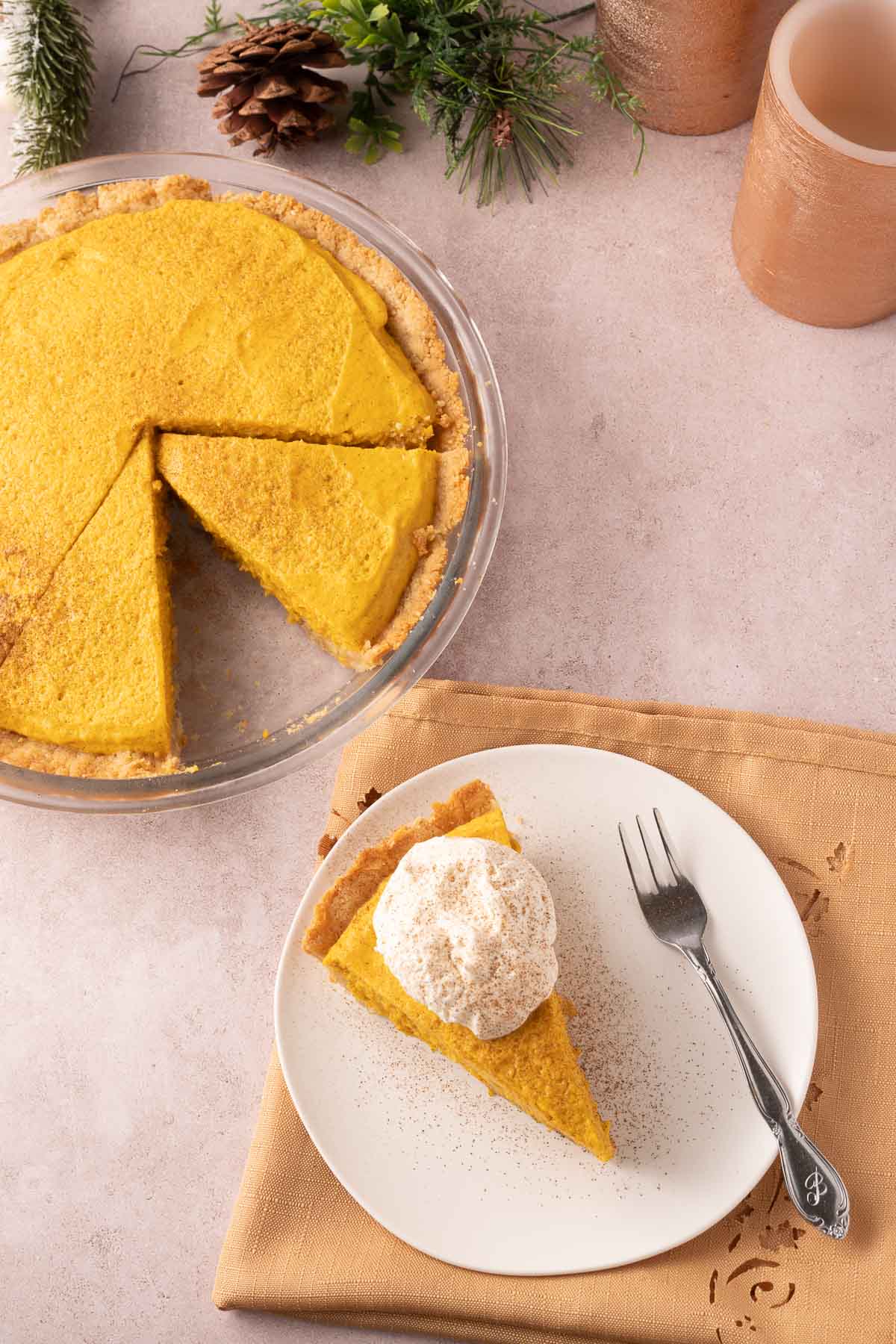 Slice of pumpkin pie with whipped cream on plate and pumpkin chiffon pie in glass pie plate.