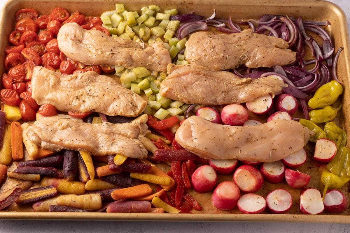 Marinated chicken slices and vegetables on a sheet pan.