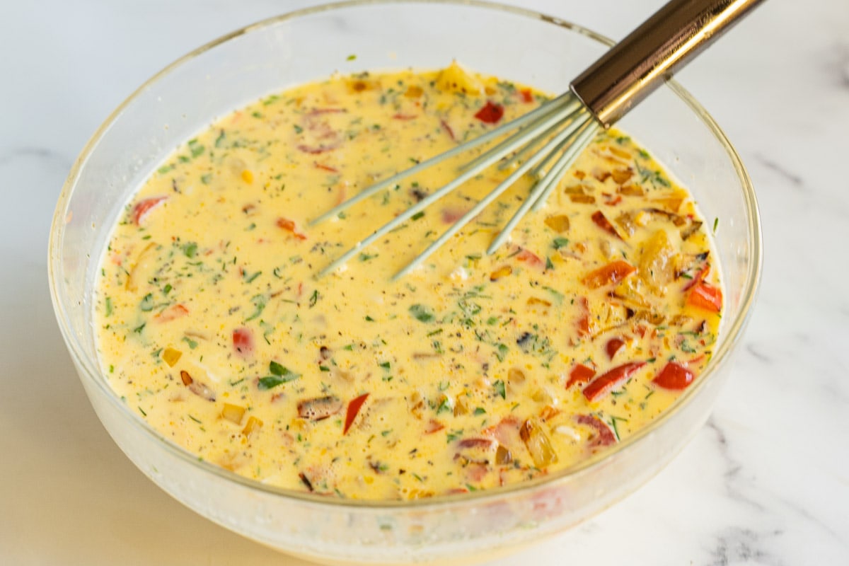Eggs, cream, vegetables, salmon, cheese mixture in glass bowl.