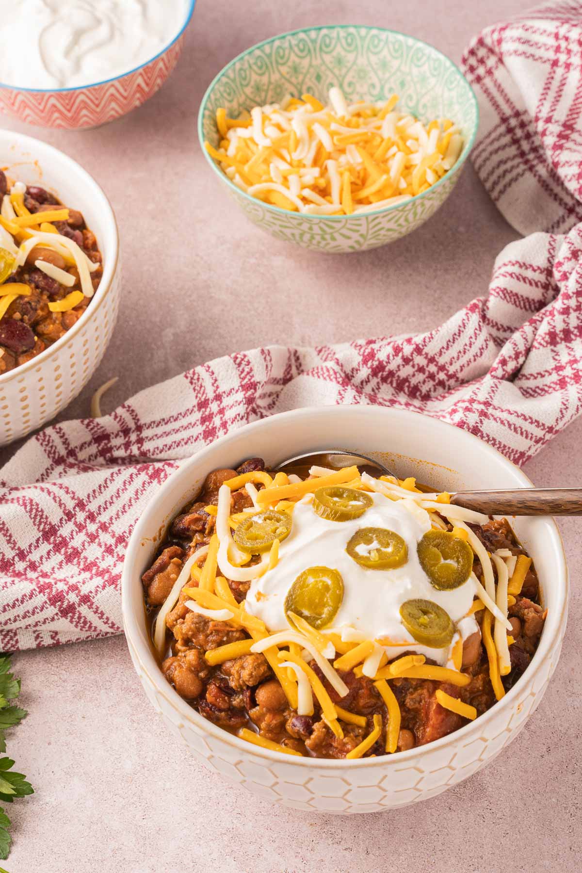 Dutch oven chili in white bowls, shredded cheese, sour cream.