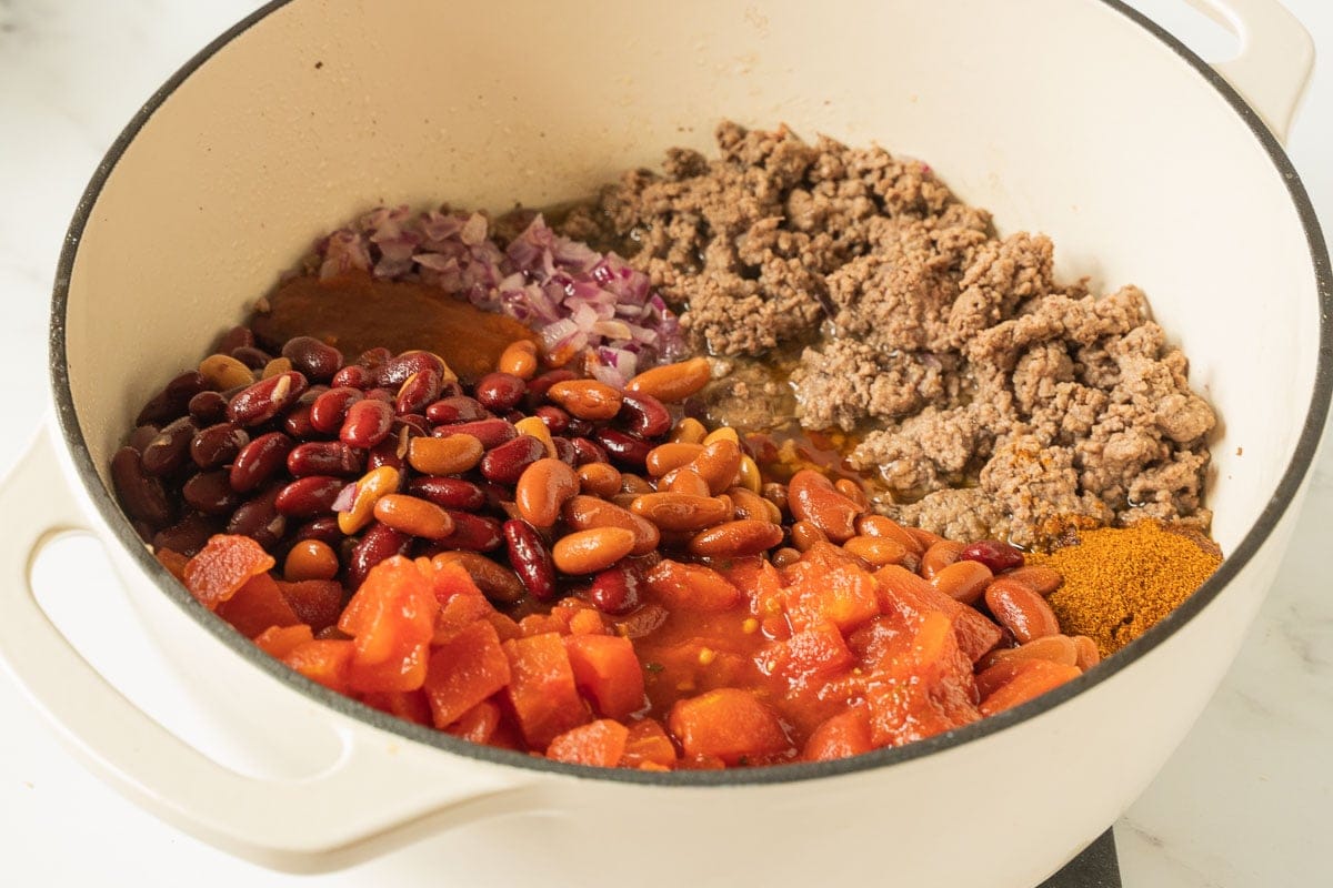 Chili bean, tomatoes, onions, ground beef in dutch oven pot.