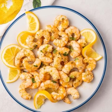 Cooked shrimp, lemon slices on white plate.