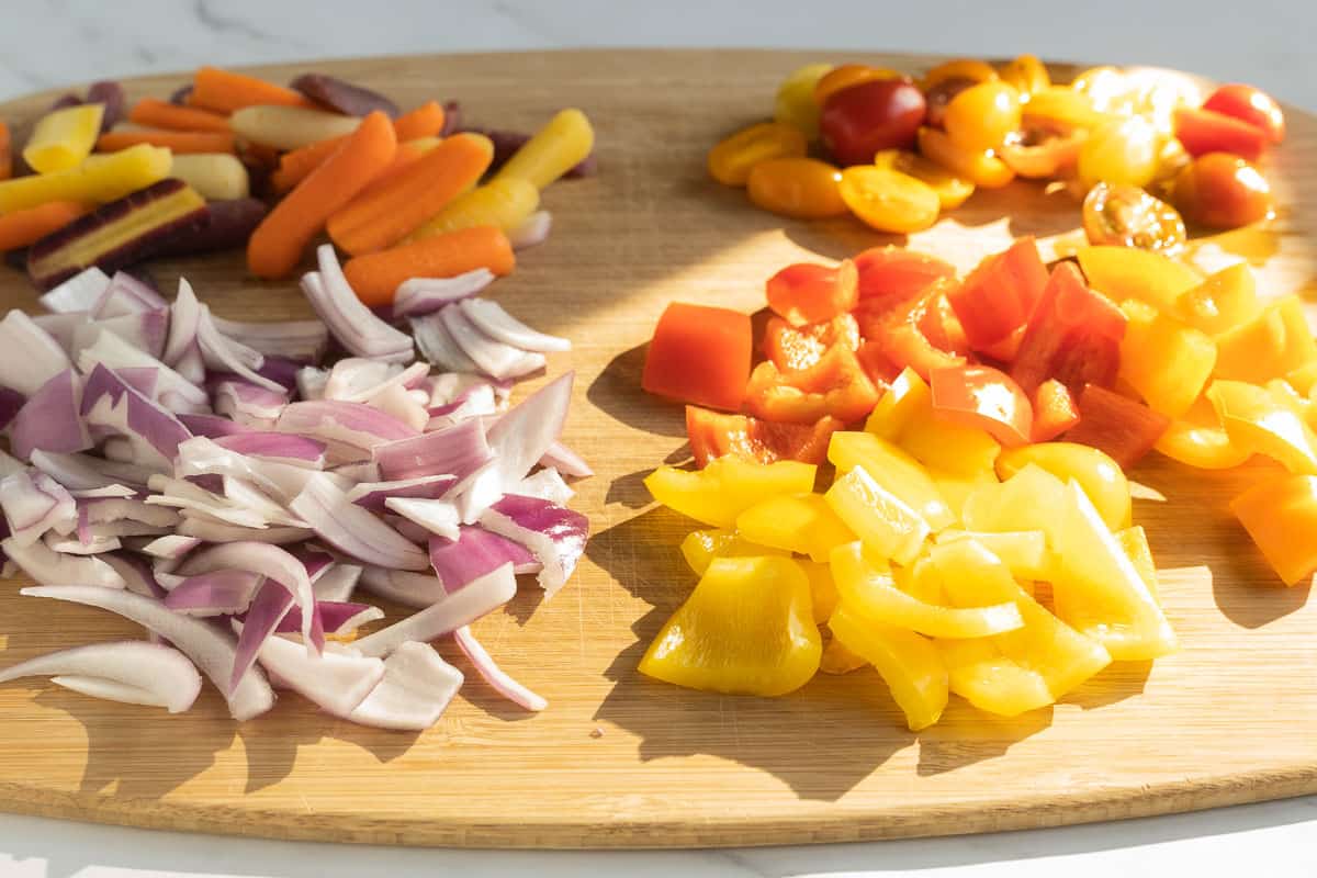 Chopped carrots, peppers, onions on wooden board.
