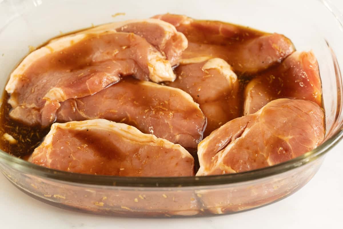 Thin sliced pork chops in marinade in glass bowl.