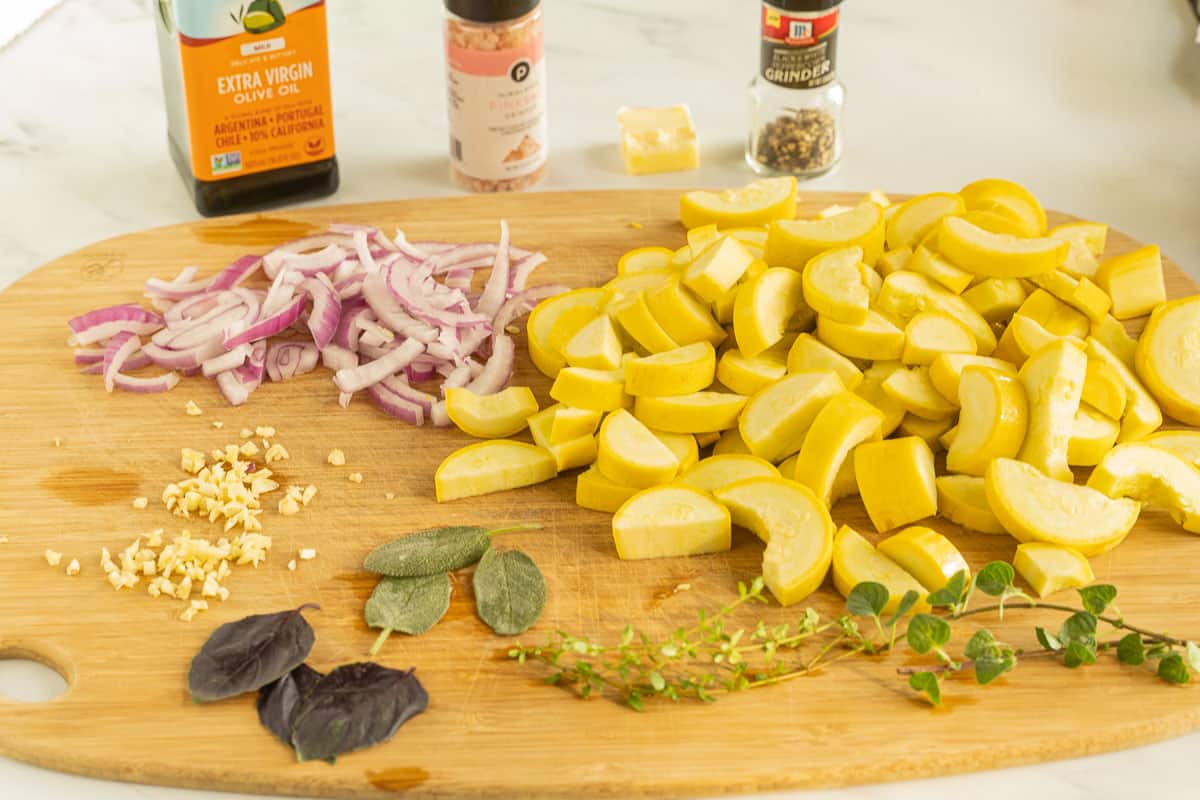 Chopped yellow squash, herbs, butter, garlic, olive oil on wooden board.