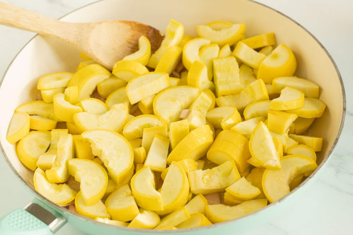 Chopped yellow squash in skillet with wooden spoon.