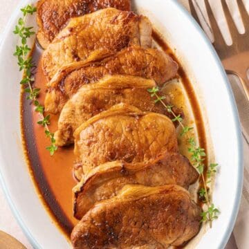Thin sliced marinated pork chops on white platter with stems of thyme.