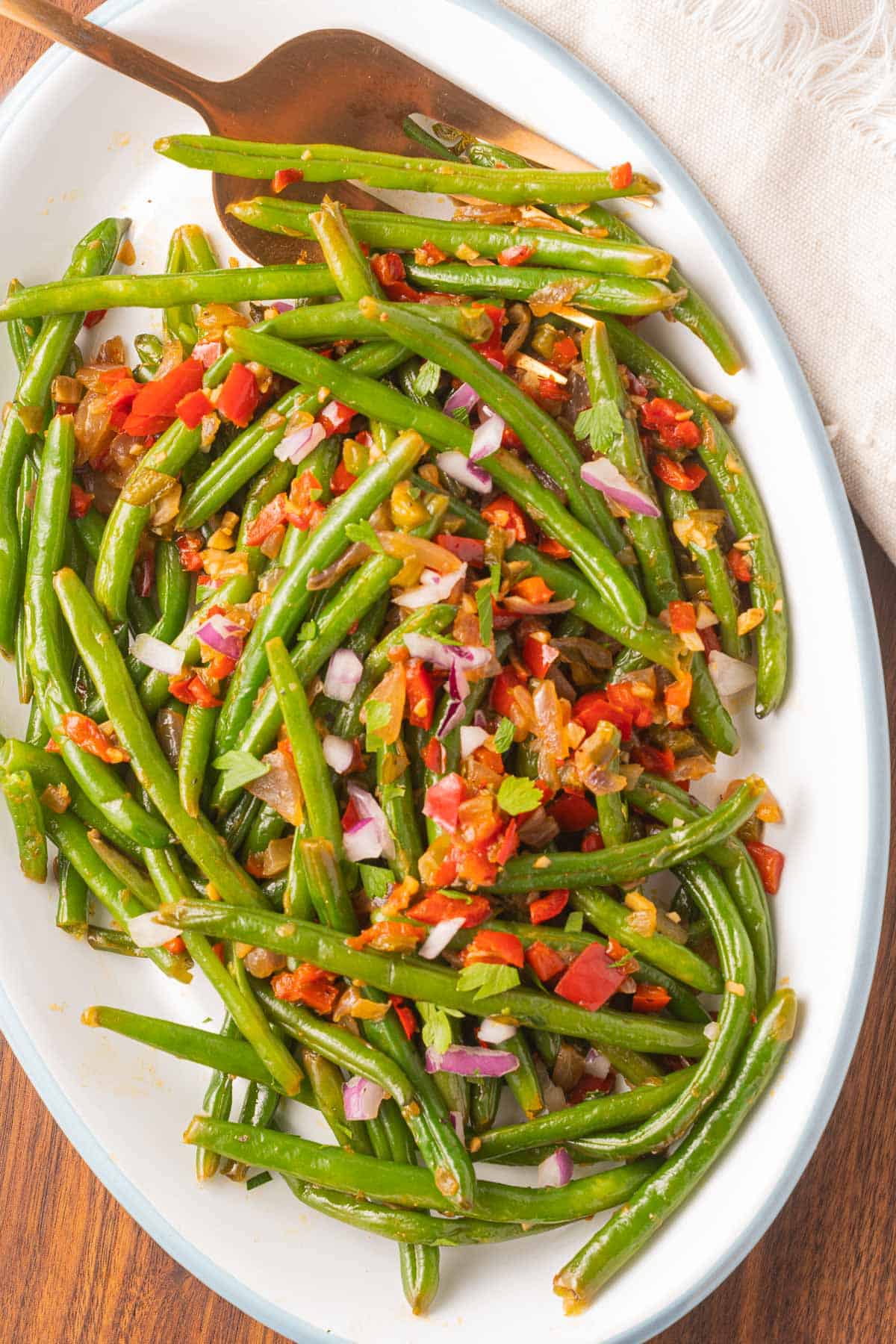 Mexican green beans, red pepper, onions on white platter with gold fork.