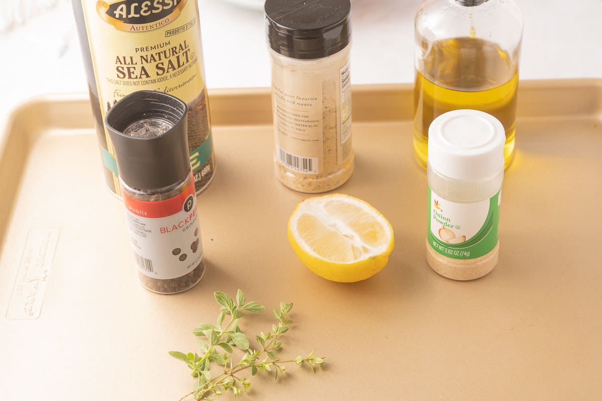 Lemon, herbs, oil, garlic, salt, pepper on a tray.