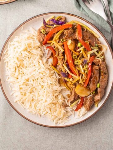 Beef chop suey and rice on plate with forks and green napkin.