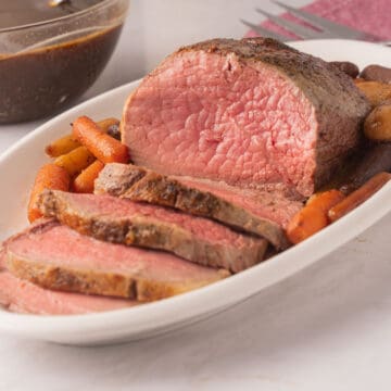 Sliced eye round roast and carrots on white platter.