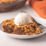 Slice of sugar free pecan pie on white plate with scoop of vanilla ice cream.