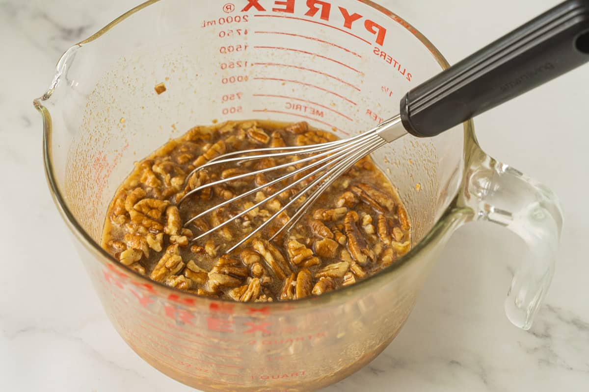 Chopped pecans, syrup, honey, butter, eggs, spices mixed in measuring cup.