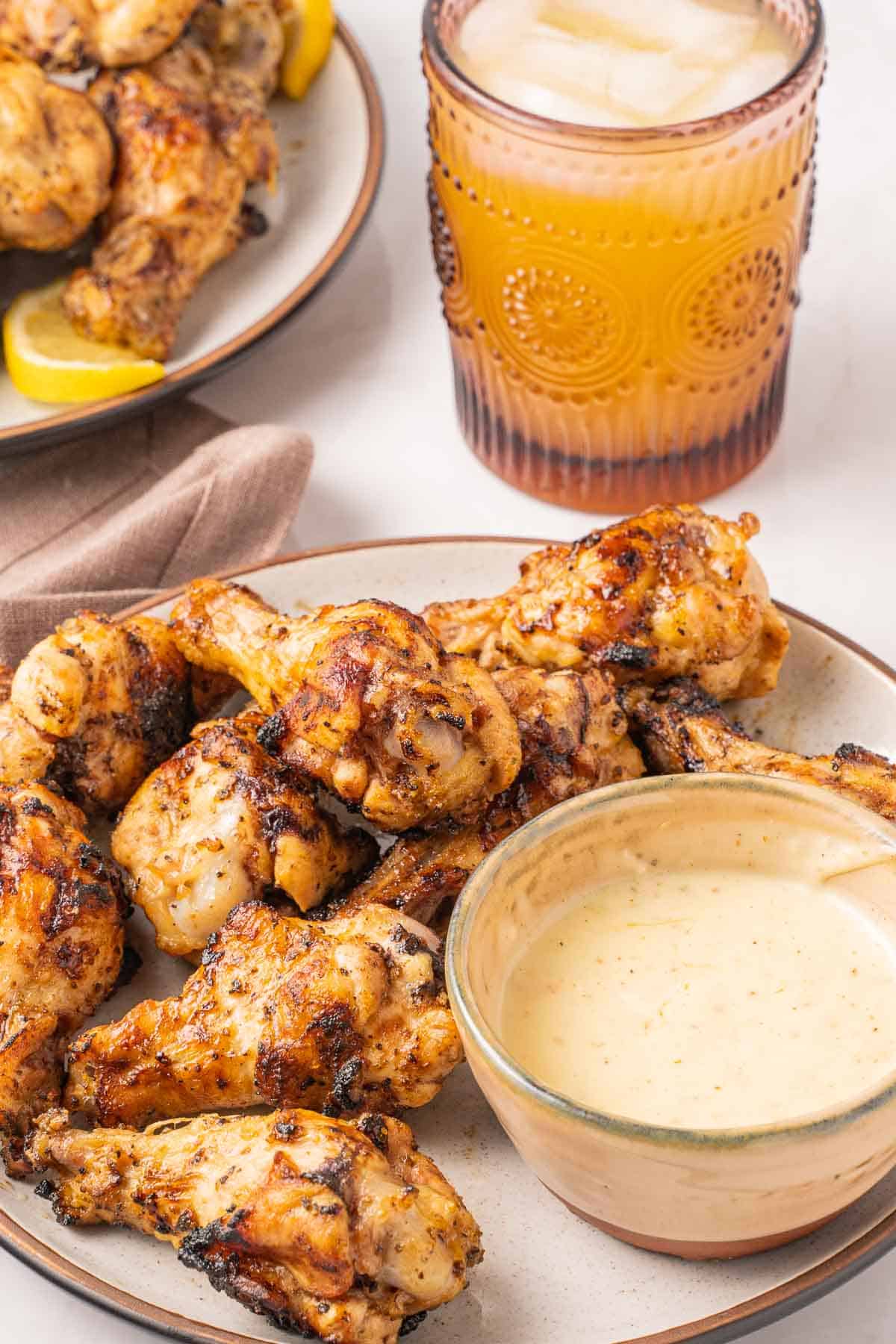 Grilled lemon pepper wings on plate with lemon sauce and glass of juice.