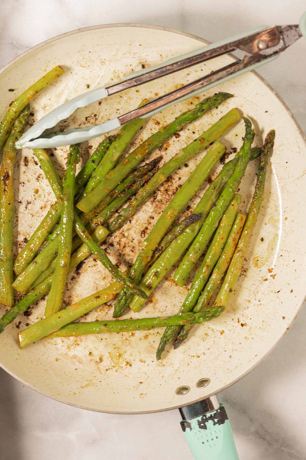 Pan seared asparagus in skillet with cooking tongs.