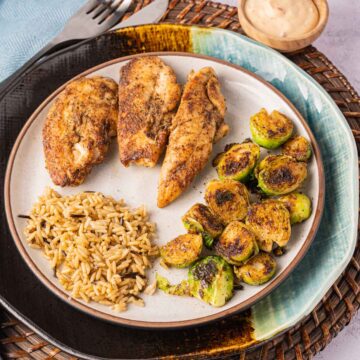 Blackened chicken tenders, rice, brussels sprouts on plate.