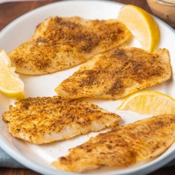 Broiled flounder fillets on white platter with lemon.