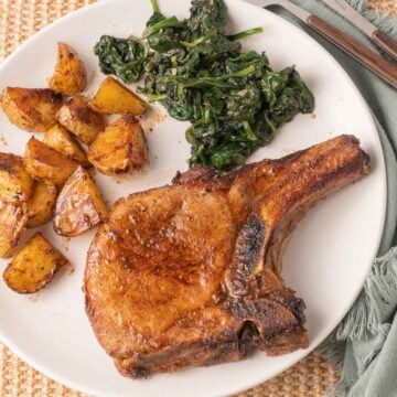 Marinated broiled pork chop with spinach and potatoes on white plate.