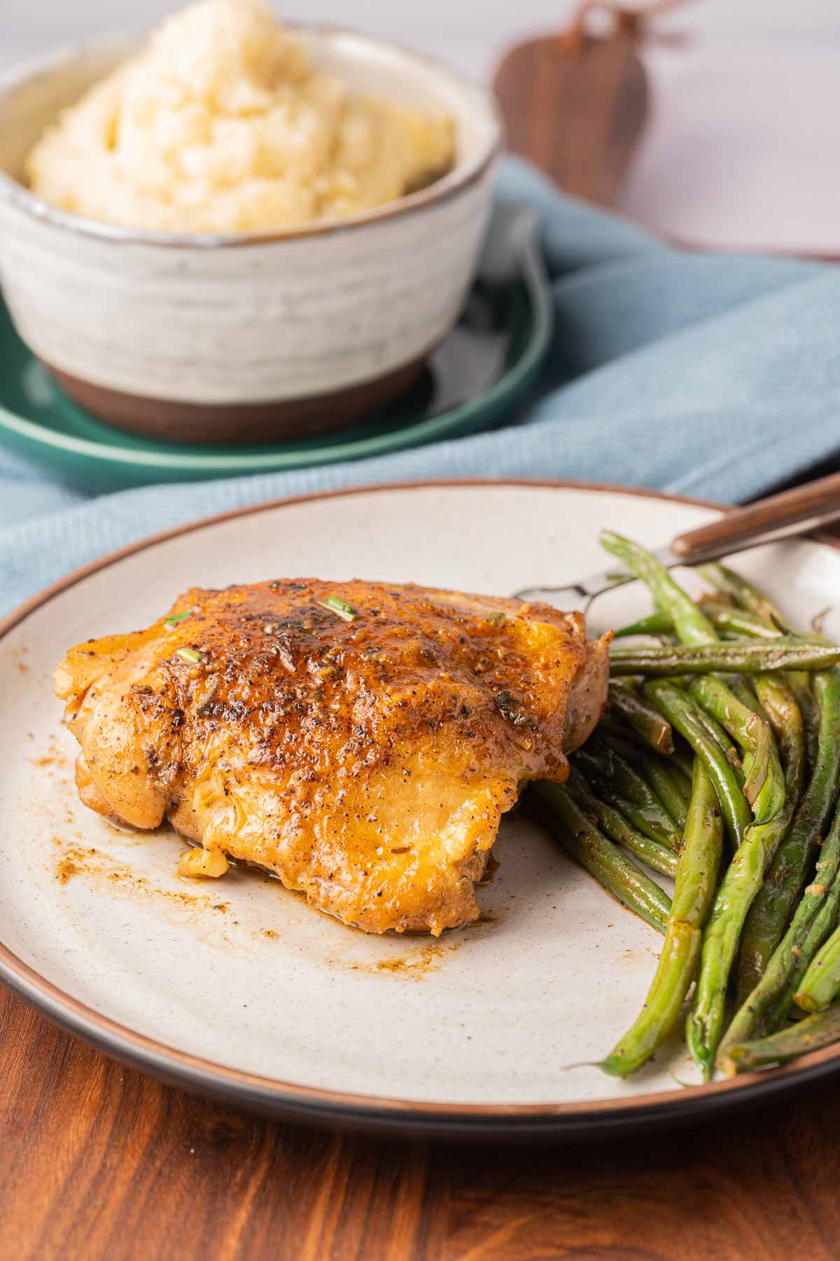 Pan Seared chicken thighs, green beans on plate with bowl of mashed potatoes.
