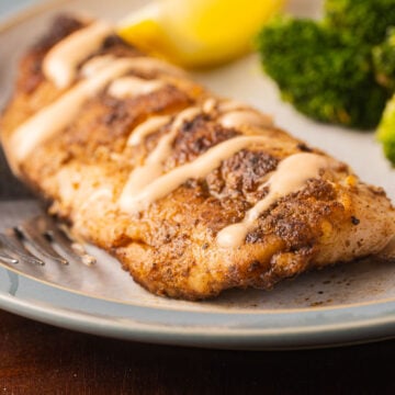 Blackened Flounder, cajun sauce with broccoli and lemon slices on plate.