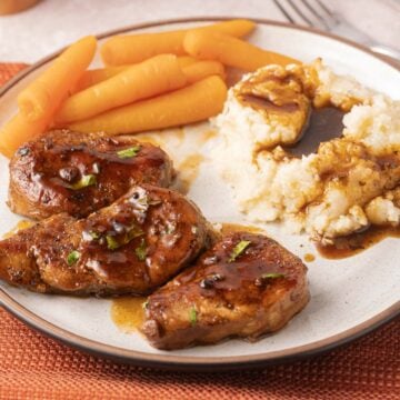 Pork tenderloin slices, mashed potatoes, gravy, carrots on plate.