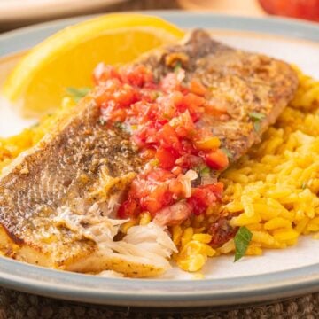 Pan fried whiting filet on yellow rice with tomato relish and lemon slice on plate.